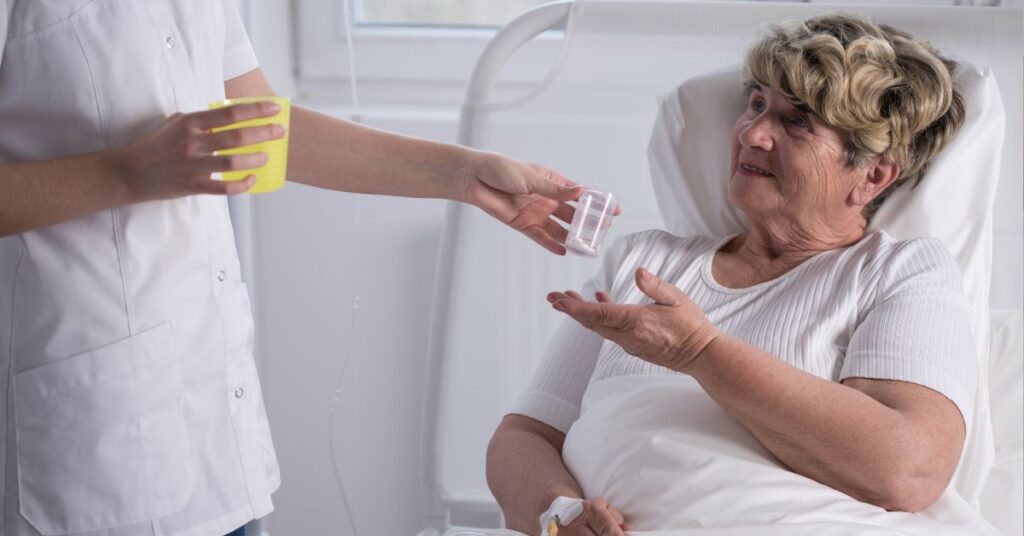 Opiekun podaje leki i napój osobie leżącej w łóżku podczas codziennej opieki i nawadniania