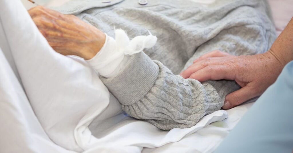 Opieka nad osobą leżącą w łóżku z podparciem kończyny i spokojnym kontaktem z opiekunem