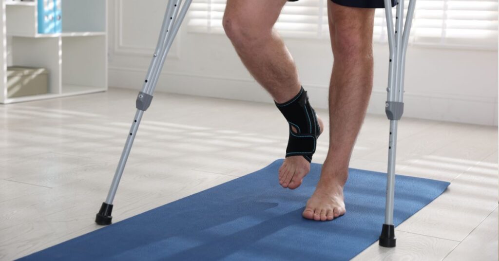 Osoba ćwiczy z ortezą stawu skokowego i kulami podczas rehabilitacji po urazie kostki