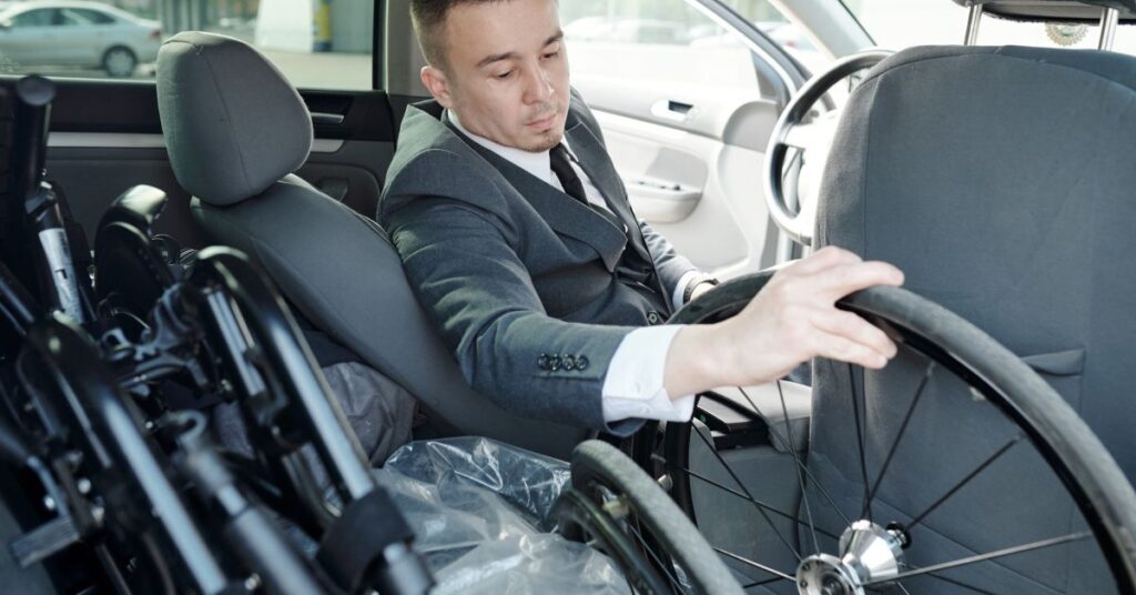 Mężczyzna wkłada koło od wózka inwalidzkiego do samochodu podczas przygotowania sprzętu do transportu